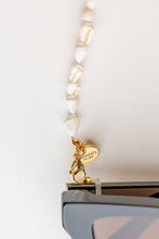 Load image into Gallery viewer, Close up BRAND The Label Logo on the seashell frame chain pictured as a sunglass chain and can be used as a necklace or wristband as part of the luxury resort wear launch collection of 2022. 
